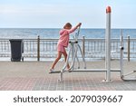 Small photo of Zelenogradsk, Russia - 07.30.2021 - Young girl in pink clothes using air walker exercise machine, sea background. Girl engaged in fitness, footwork. Outdoor sport exercises and fresh sea air