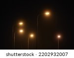 Small photo of Night lampposts shines with faint mysterious yellow light through evening fog. Streetlights shine at quiet city night, magic atmospheric light in mystical darkness
