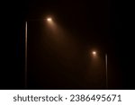 Small photo of Two night lampposts shines with faint mysterious yellow light through evening fog. Streetlights shine at quiet city night, magic atmospheric light in mystical darkness