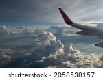 wing of airplane in sky above  clouds background of blue sky white and grey puffy clouds sky scape airplane wing in top left corner of horizontal format leaving space for type for travel vacation 