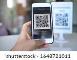 Women's hand uses a mobile phone application to scan QR codes in stores that accept digital payments without money and plastic tags on the table. QR code payment and cash technology concept