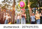 Small photo of Portrait of small girl smash a pi–ata with a bat with friends and presents outdoors in garden in summer. Happy birthday concept