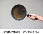 Caucasian male hand holding an old frying pan stained with brown burned oil and grease isolated on gray.