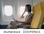 Small photo of Young female listening favourite songs during flight in first class cabin using mobile playlist and accessory, woman entertaining on airplane board enjoying music in headphones from smartphone