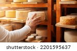Small photo of male, man cheese maker businessman, individual entrepreneur, checks cheese in cellar, basement. cheese head ripens on wooden shelves, process of producing homemade. Touches