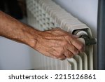 White heating radiator hanging on white wall, close up view. Person turns on or turns off radiator. Heating is getting more expensive, save money. Energy crisis.