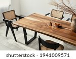 Interior design of stylish dining room interior with family wooden table, modern chairs, plate with nuts,  salt and pepper shakers. Concrete floor. White wall. Template.