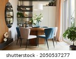 Stylish composition of elegant dining room interior design with velvet armchairs, design rouded wooden table and beautiful personal accessories. Glamour interior design inspiration. Template.