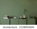 Modern living room interior composition with modern home decorations and personal accessories on the eucalyptus wooden commode. Sage green wall. Template. Copy space.