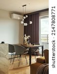 Small photo of Modern and vintage dining room with brown wooden table, grey chairs and stylish chandelier. Minimalistic white wall and brown curtains. Creative accessories. Herringbone wooden parquet. Template.