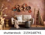Small photo of The stylish boho composition at living room interior with design beige sofa, coffee table, wicker baskets and elegant personal accessories. Brown and white pillows and plaid Cozy apartment. Home decor