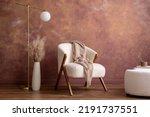 Boho composition a living room interior with white boucle  armchair, design pouf, lamp, vase with dried flowers, gold lamp and personal accessories. Cozy home decor. Template. Copy space.