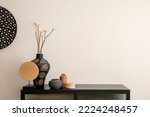 Minimalist composition of living room interior with copy space, black commode, vase with dried flowers, decoration on the wall and stylish personal accessories. Home decor. Template. 