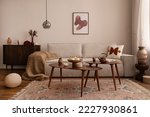 Domestic and cozy interior of living room with mock up poster frame, modern beige sofa, oval wooden coffee table, round pillows, braided plaid, vintage rug, wooden floor, lamp and personal accessories