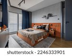 Small photo of Interior design of elegant bedroom with big orange bed, beige and grey bedclothes, blue curtain, rug, modern lamp, night stand, vase with dried flowers and personal accessories. Home decor. Template.