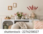 Interior design of easter living room interior with mock up poster frame, stylish white sideboard, hyacinth, easter bunny, vase with dried flowers and personal accessories. Home decor. Template.