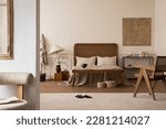 Small photo of Cozy composition of bedroom interior with mock up poster frame, stylish bed, beige bedding, rattan armchair, bright rug, round box, slippers, lamp and personal accessories. Home decor. Template.