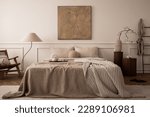 Cozy bedroom interior with mock up poster frame, big bed, beige bedding, plaid, lamp, wooden stands, black ladder, beige rug, wall with stucco and personal accessories. Home decor. Template.