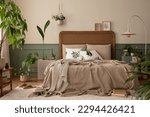 Small photo of Warm and cozy bedroom interior with mock up poster frame, boho bed, beige bedding, green wall with stucco, books, brown slippers, plants in pots and personal accessories. Home decor. Template.