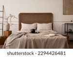 Small photo of Creative composition of bedroom interior with cozy bed, beige bedding, plaid, trace with pitcher and cup, coffee table with branch, black ladder and personal accessories. Home decor. Template.