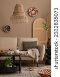 Small photo of Creative composition of boho living room interior with beige sofa, black round coffee table, boho lamp, partition wall, plaid, colorful basket on wall and personal accessories. Home decor. Template.