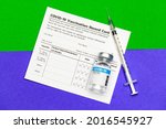 Small photo of Medical injected syringe and sealed glass capsule of covid-19 vaccine on vaccination record card put across borderline of green and purple area looks as immunity safe and infection risk zone
