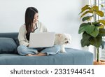 Small photo of sian young happy cheerful female owner sitting smiling on cozy sofa couch using browsing surfing internet shopping online via laptop computer with best friend white dogs mutt shih tzu.
