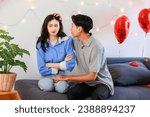 Small photo of Millennial Asian young romantic cheerful lover couple male boyfriend try to sorry reconcile angry female girlfriend sitting hugging cuddling smiling on cozy sofa celebrating valentine day together.