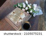 Small photo of A broken gravestone made of granite with artificial flowers, a desecrated grave, a profanation of a cemetery. The concept of disrespect for the dead and for memory