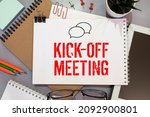 Small photo of kickoff meeting, text on notepad sheet on brown background near magnifier and coffee cup.