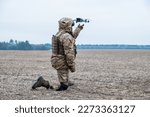 Ukrainian army soldier kneels in a field and launches a quadcopter into the sky. The soldier is dressed in military fatigues and wears a helmet with a face shield.