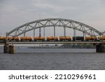 Riga railway bridge over the Daugava River with iron arch and oil tank wagons travelling over the bridge and Riga radio and tv tower in the background