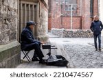 Small photo of Central District, Riga, LV-1050, Latvia October 2nd 2022 A male busker playing a keyboard on the doorstep of an old church in Riga Old Town as a man walks past