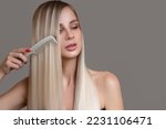 beautiful young woman holds a comb in her hands. Blonde woman with long straight hair on a gray background