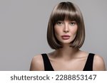 Small photo of Portrait of beautiful fashion woman with bob hairstyle. Thick short wig. Gray background