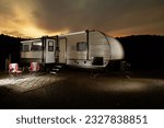 Travel trailer at dusk  with a bright yellow sunset behind a silhouetted ridgeline with trees