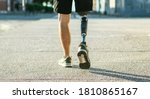 Small photo of Low angle view at disabled young man with prosthetic leg walking along the street