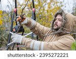 Small photo of Male gardener prune fruit tree using battery powered pruning shears, secateur. Pruning electric tools. Farmers prunes and cuts branches of a tree in the garden with electric pruning shears or secateur