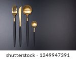 Set of stylish black and gold cutlery on black background. Dark and moody vibes. Fashionable and luxury eating. Flat-lay, top view. Copy space for your text.