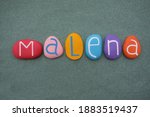 Small photo of Malena, female given name composed with multi colored stone letters over green sand