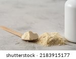 Small photo of Pile of bovine colostrum powder with wooden spoon and white container on white background. Colostrum benefits for immune system and gut health concept