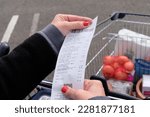 Small photo of Vannes, France, march 29, 2023 : Purchasing power concept with a till receipt close up and a full supermarket trolley in the background