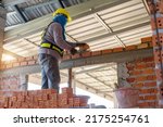 Small photo of Builder carefully puts red brick on the masonry. Quick work bricklayer. Guy measures level masonry. Man is building brick wall. Correctly calculate material. Builder manually carries brick structure,B