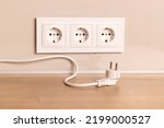 Small photo of Power cord cable unplugged with group of white european electrical outlets on modern beige wall
