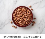 Raw peanut seeds in a wooden bowl on a marble countertop. Dried peeled groundnut as healhy vegetarian snack. Whole organic monkey nut for dietary nutrition. Arachis hypogaea fruits. Top view.