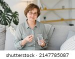 Small photo of Mature senior middle aged woman holding pill and glass of water taking painkiller to relieve pain, medicine supplements vitamins, antibiotic medication, meds for old person concept, close up view