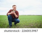 Small photo of Young handsome farmer with tablet squatting in corn field in spring. Agribusiness and innovation concept.