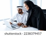 Man and woman with traditional clothes working in a business office of Dubai. Portraits of  successful entrepreneurs businessman and businesswoman in formal emirates outfits. 
