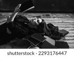 Small photo of A relaxed woman underlie and reads in a room full of books. Black and white.