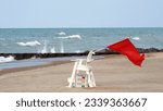 Small photo of Red flag waves from a lifeguard chair as a warning during a closure at Kenilworth Beach on the Lake Michigan shore. Red flag is high hazard meaning high surf or strong currents.